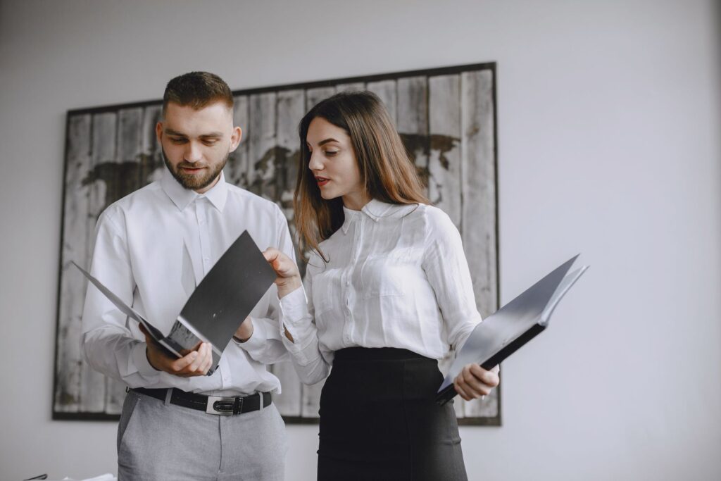 Two office colleagues compare documents in separate folders.