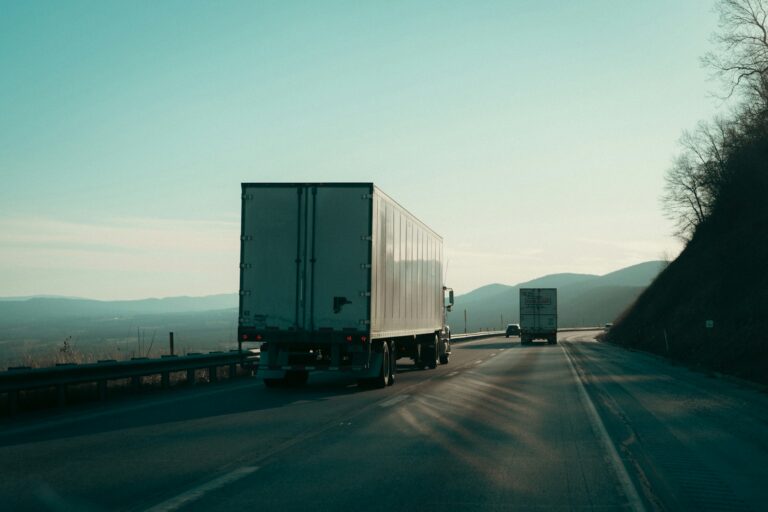 Two semi trucks traveling along a highway near mountains
