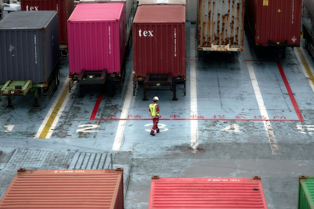 Worker walking between shipping containers at a cargo terminal
