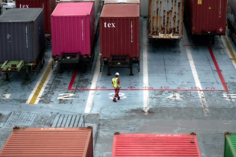 Worker walking between shipping containers at a cargo terminal